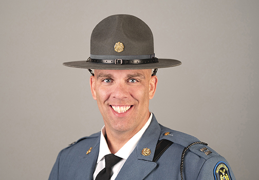Smiling male police officer in blue uniform and gray campaign hat with badge.