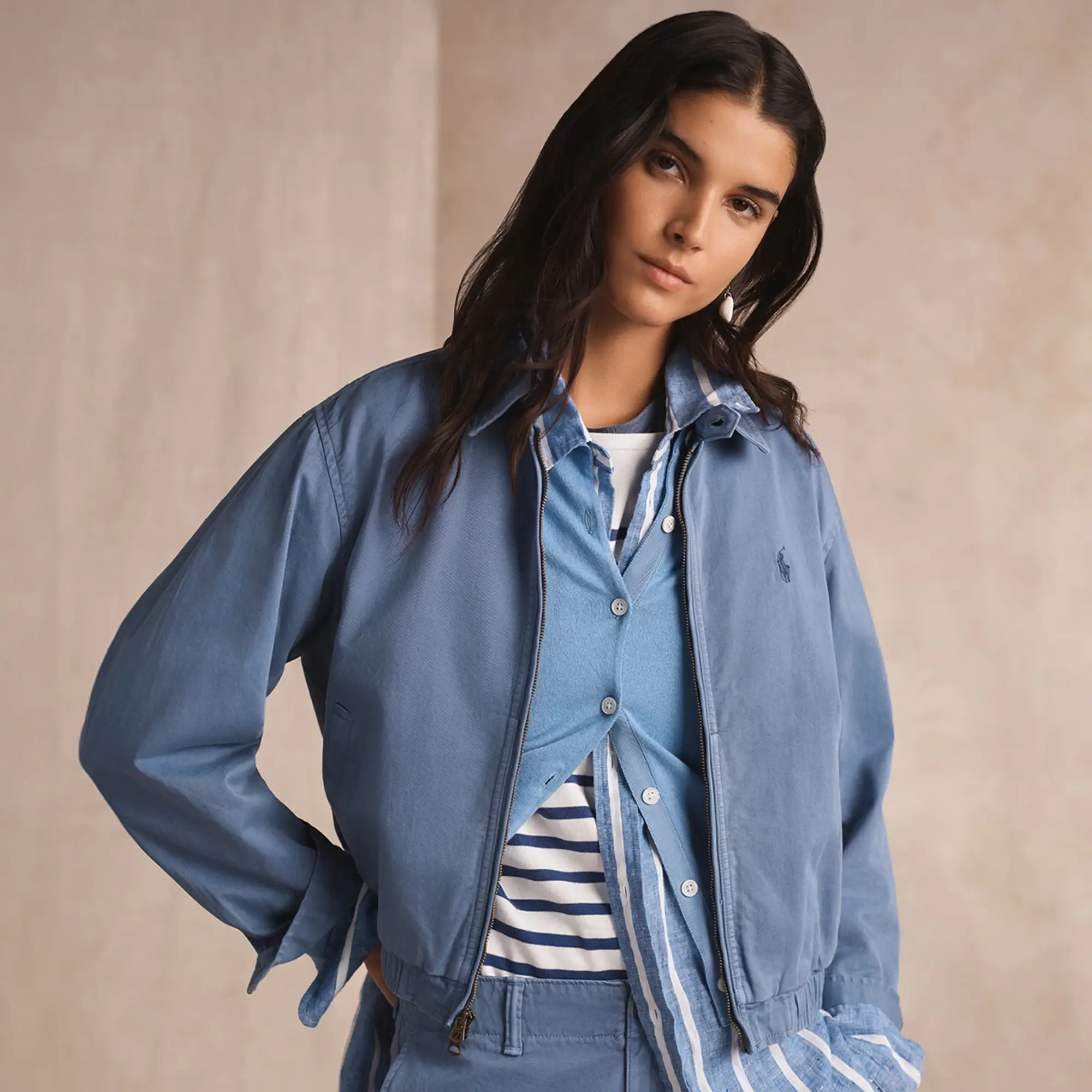 Person wearing layered blue outerwear over a striped shirt, standing against a neutral backdrop.