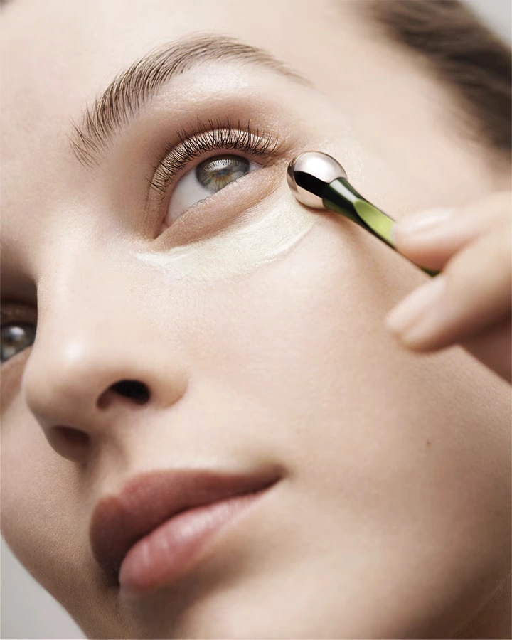 Close-up of a person applying eye cream under the eye using a green applicator tool.
