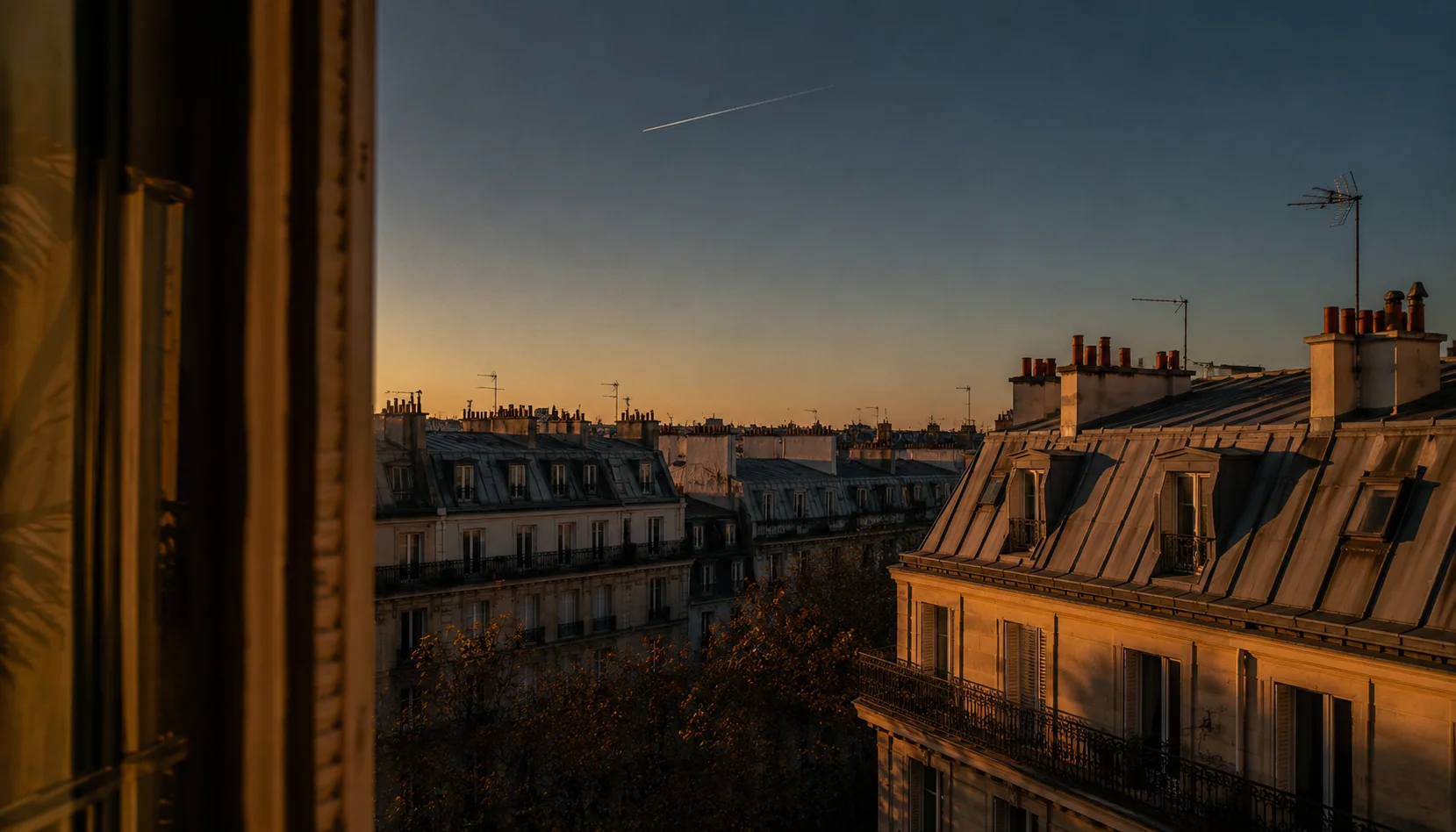 Toits parisiens en zinc et façades haussmanniennes éclairés par la lumière dorée du soir.