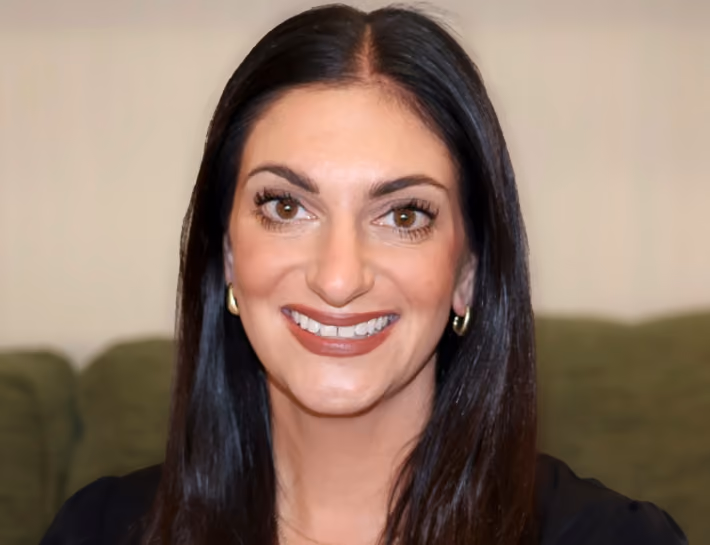 Smiling woman with long dark hair, brown eyes, wearing gold hoop earrings and a black top.