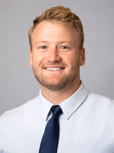 Smiling woman with long curly blonde hair wearing clear-framed glasses and a blue top.