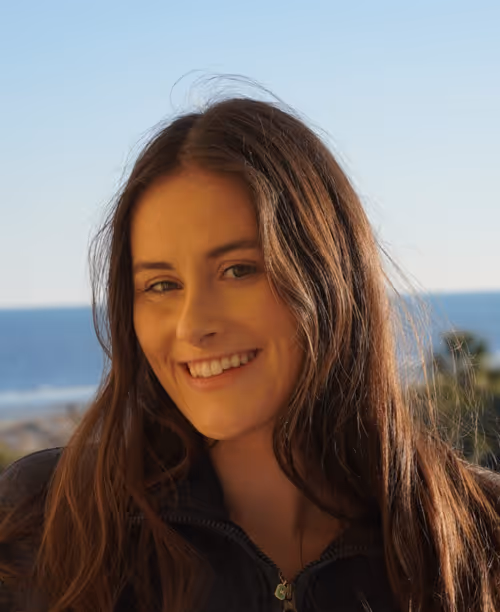 Smiling woman with long curly blonde hair wearing clear-framed glasses and a blue top.
