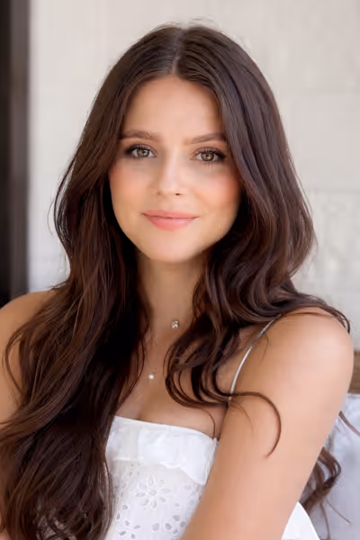 Smiling woman with long curly blonde hair wearing clear-framed glasses and a blue top.