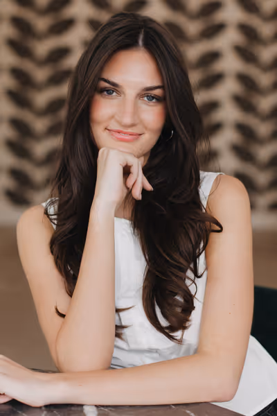 Smiling woman with long curly blonde hair wearing clear-framed glasses and a blue top.