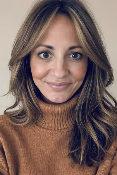 Smiling woman with long curly blonde hair wearing clear-framed glasses and a blue top.