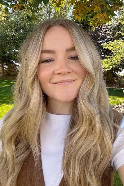 Smiling woman with long curly blonde hair wearing clear-framed glasses and a blue top.