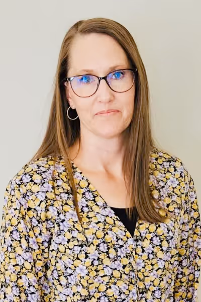 Smiling woman with long curly blonde hair wearing clear-framed glasses and a blue top.