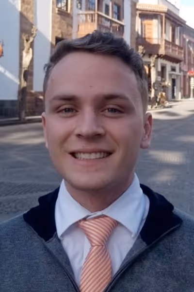 Smiling woman with long curly blonde hair wearing clear-framed glasses and a blue top.