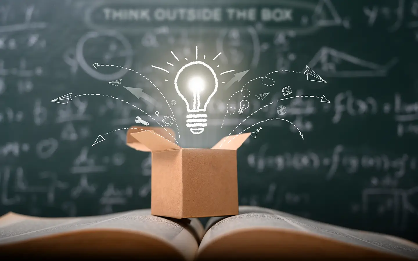 A light bulb, box, and book in front of a blackboard representing creating education