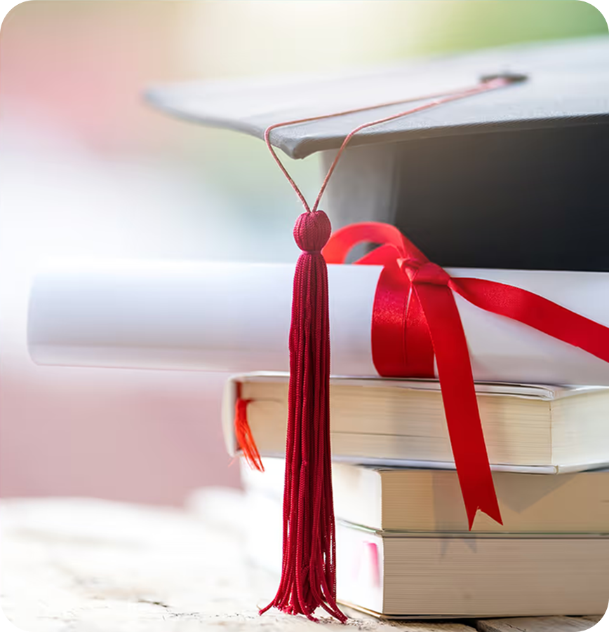 Graduation cap with red tassel resting on top of a stack of books and a diploma tied with a red ribbon.