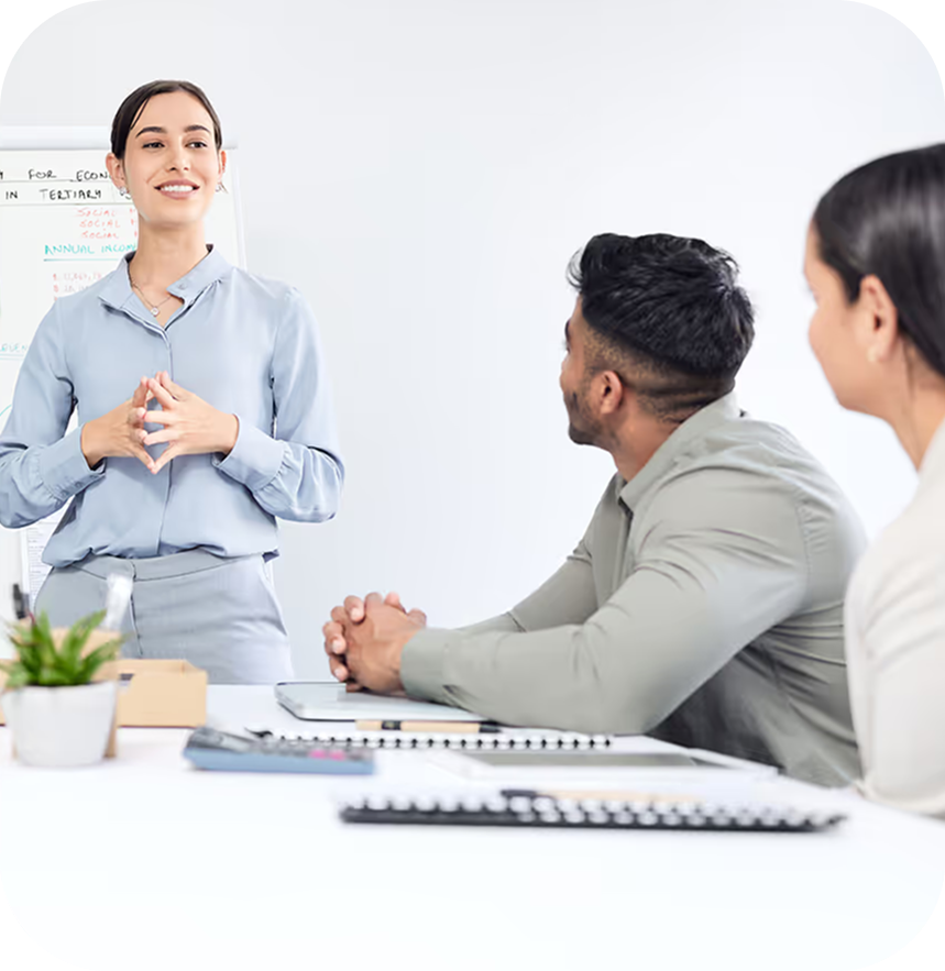 Woman standing and speaking to two seated colleagues in a bright office setting.