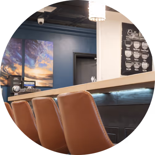 Bar counter with brown leather chairs, blue wall with artistic sky painting, and a coffee-themed poster.