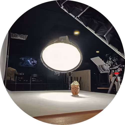 Food photography setup with a dessert glass topped with whipped cream on a table under a large studio light and a camera on a tripod.