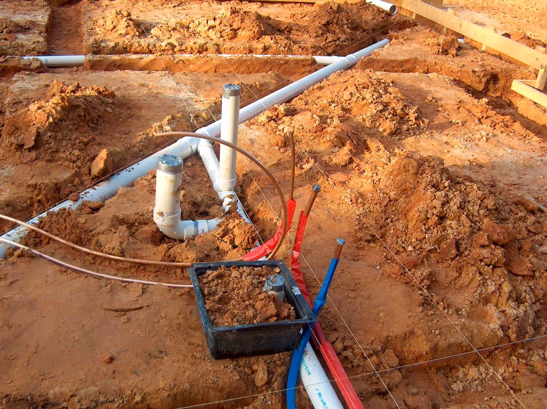 Construction site with plumbing pipes and electrical conduits in dirt ground