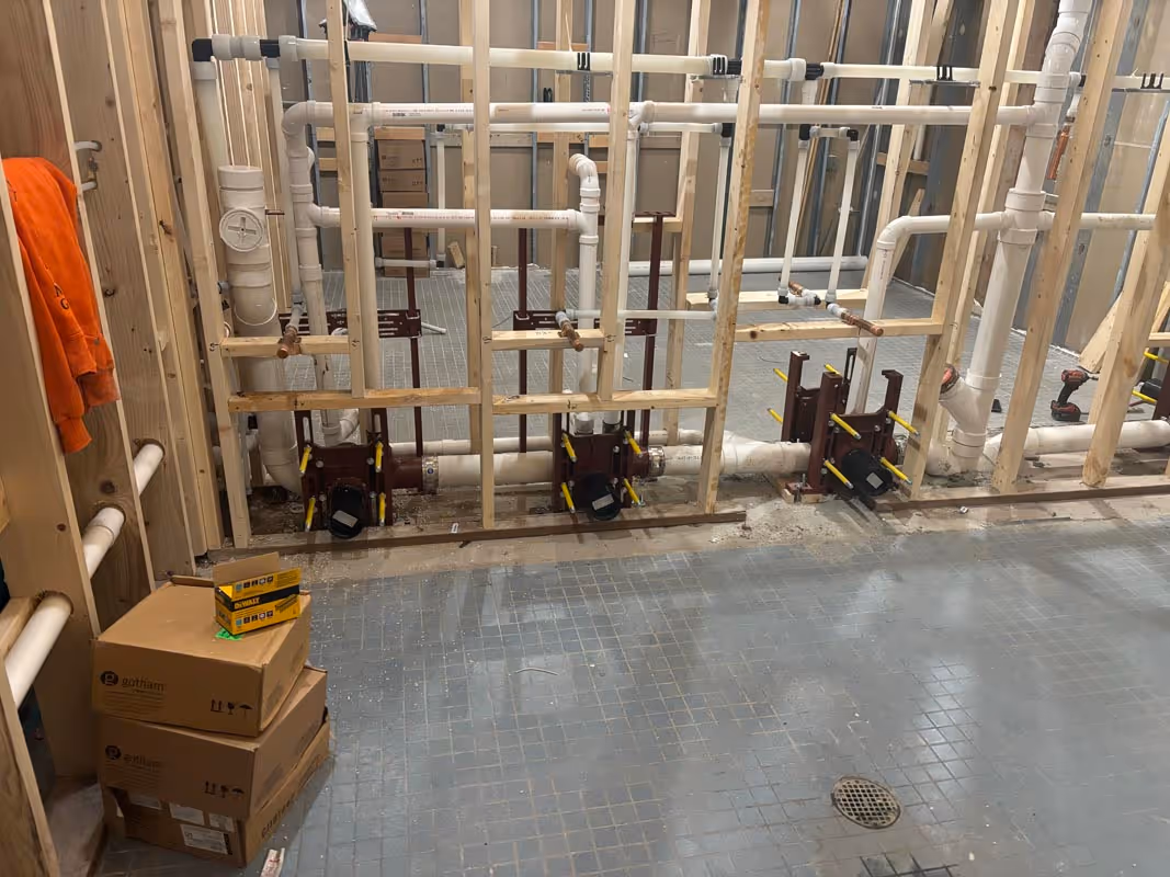 Plumbing rough-in with white pipes, wooden framing, and cardboard boxes