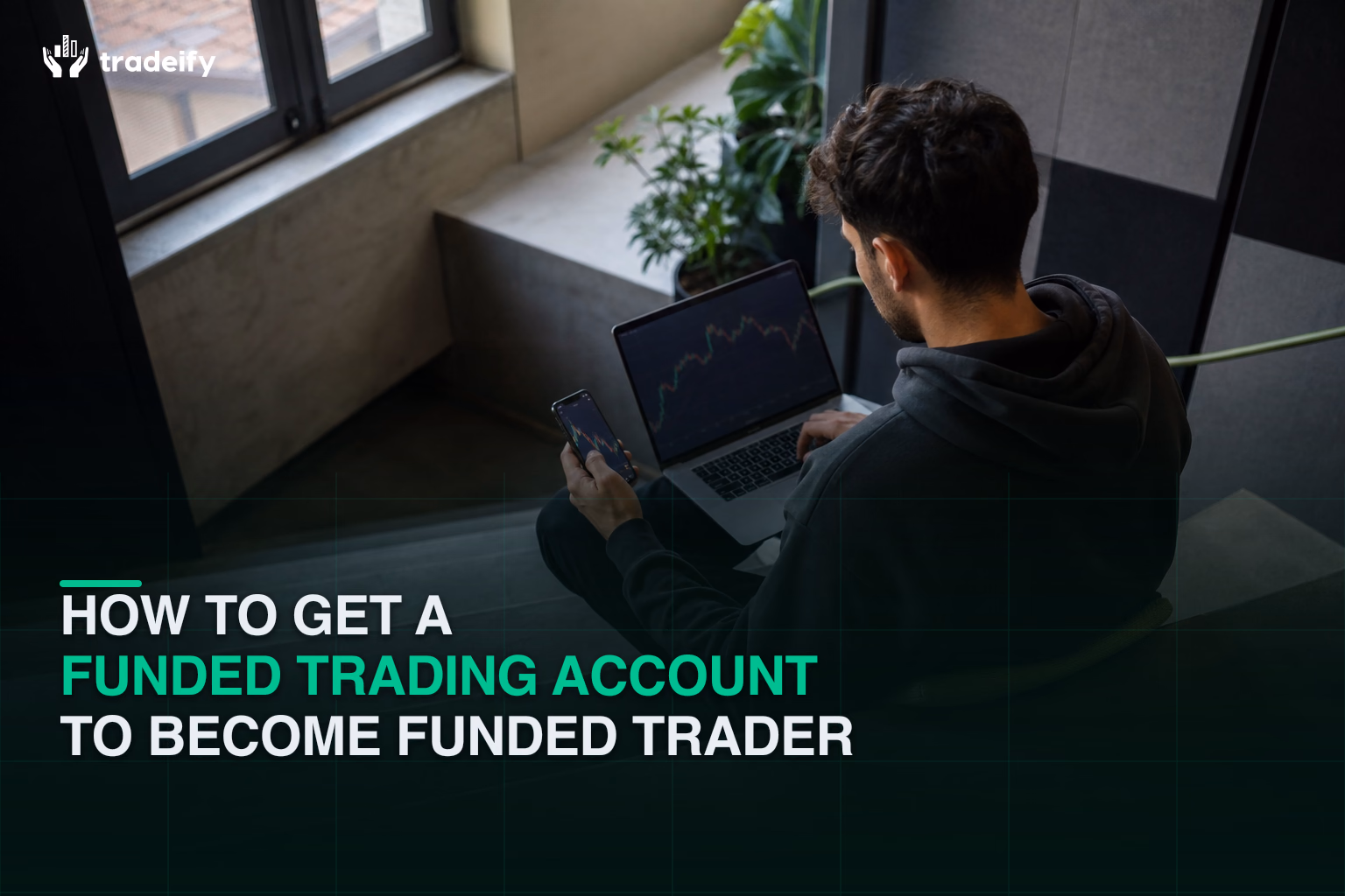 Young trader comparing funded trading account rules on a laptop and phone in a contemporary coworking stair lounge