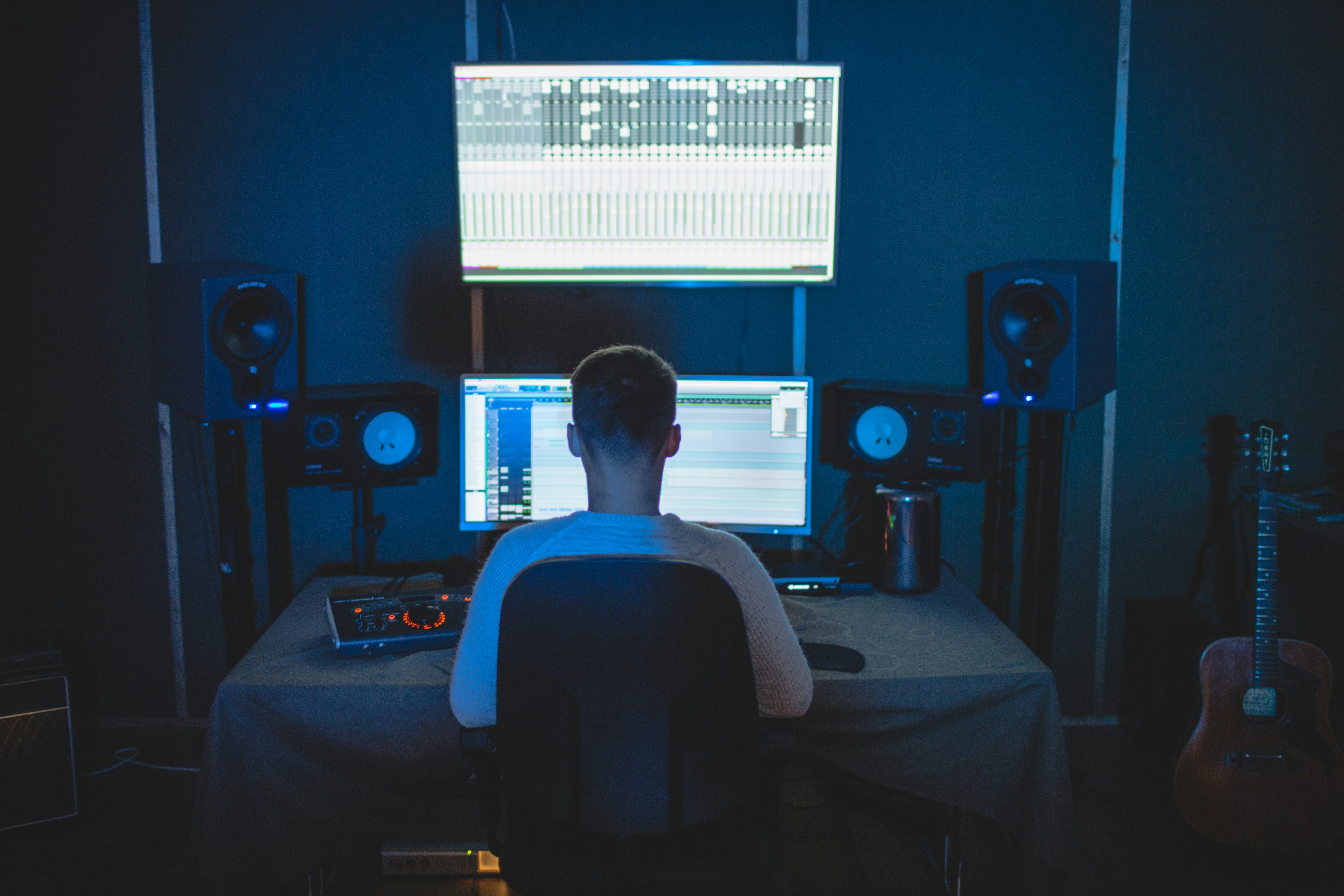 Photo of a man sitting at his music studio desk with multiple studio monitors