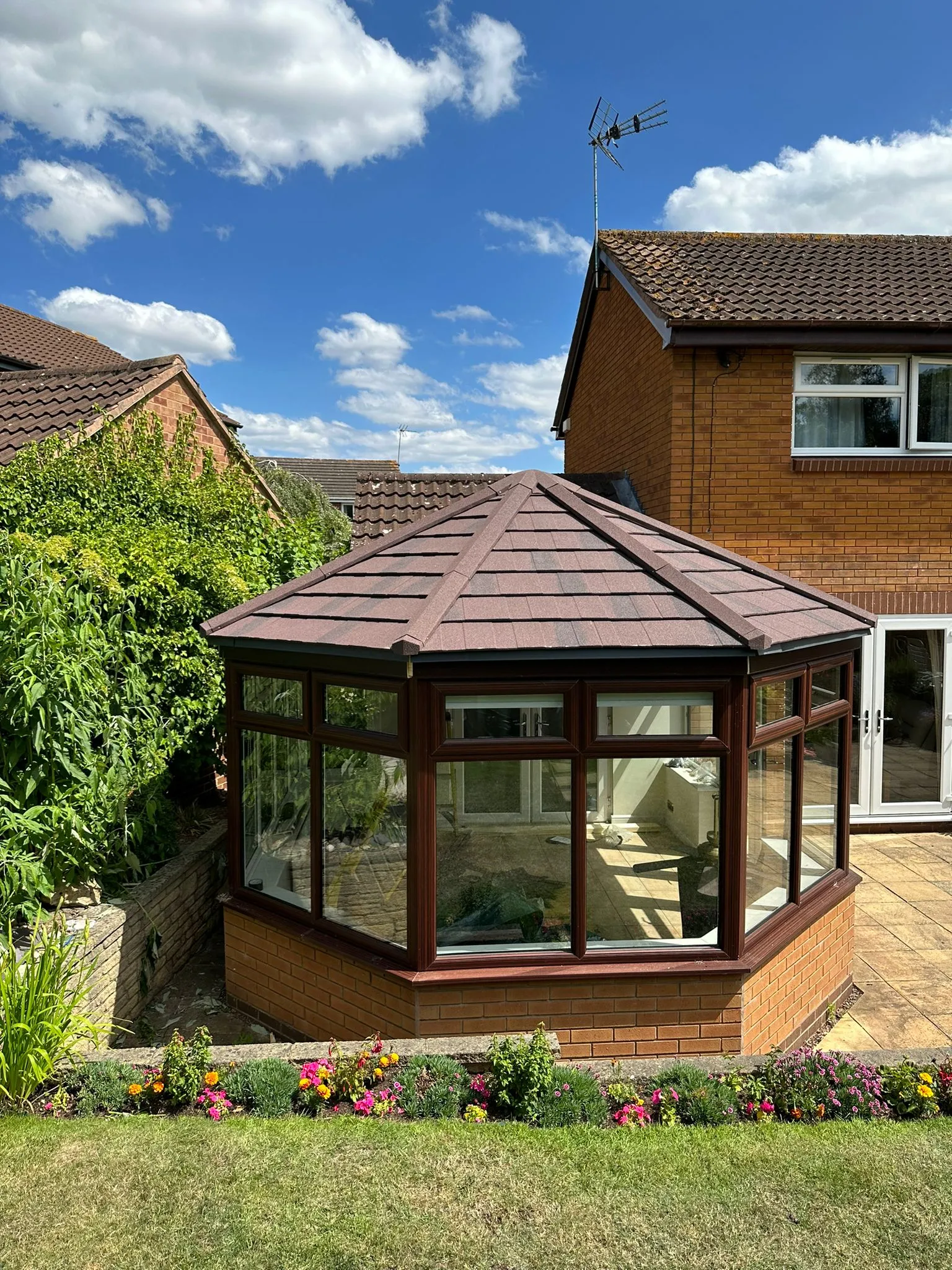 Rosewood uPVC Victorian conservatory with a tiled roof overlooking a garden lawn