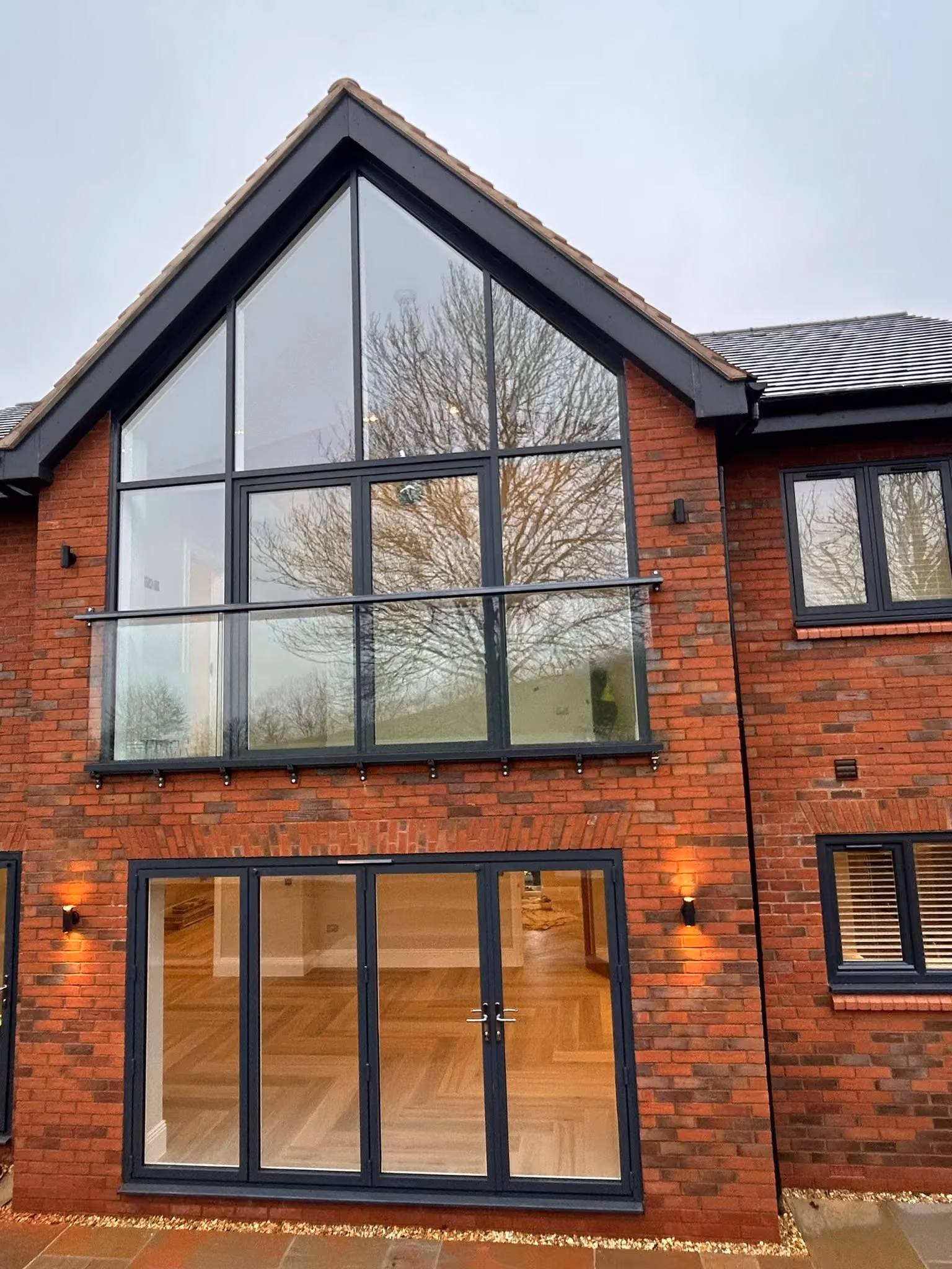 Red-brick house with large grey aluminium framed windows and bifold doors