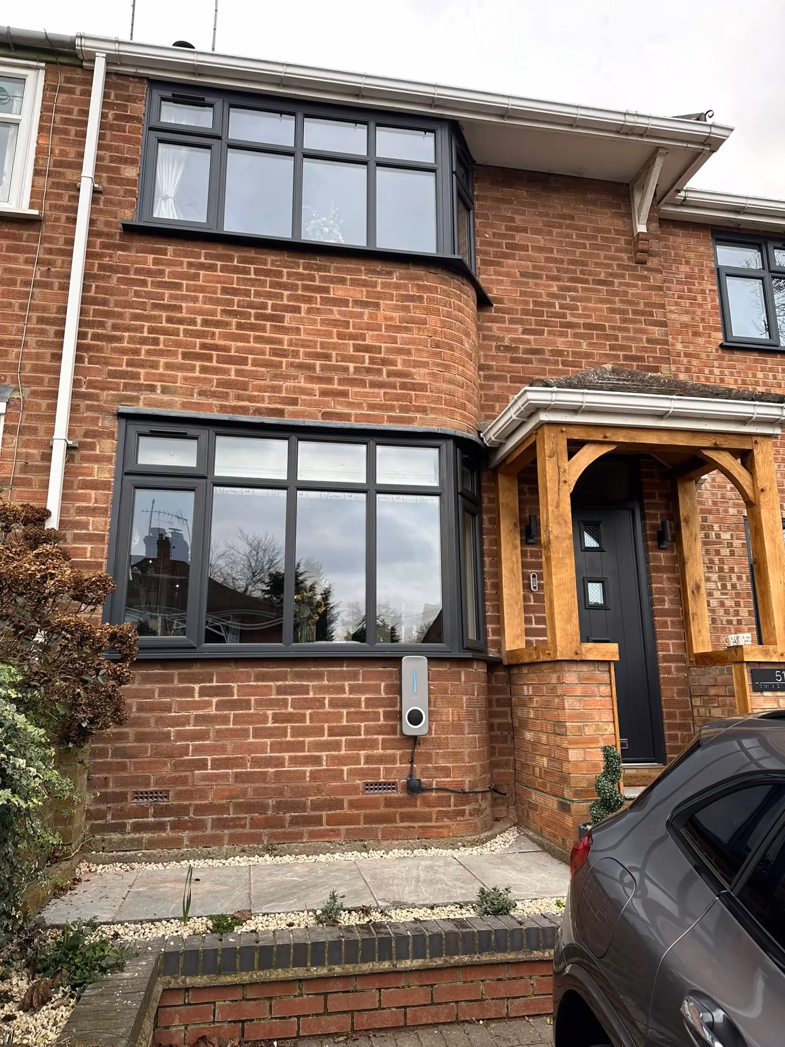 House with black-framed bay windows, a wooden porch over a black front door