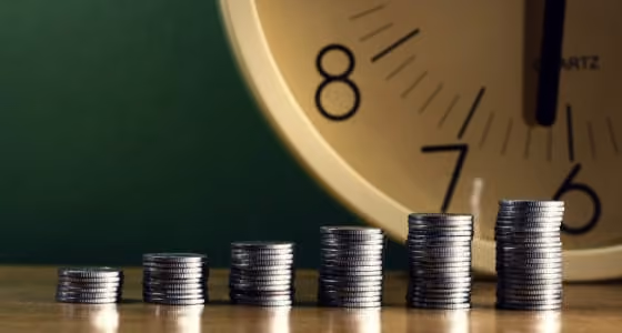 Several stacks of coins increasing in height from left to right with a clock in the background