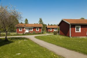 Tre röda stugor och grön gräsmatta med blommor