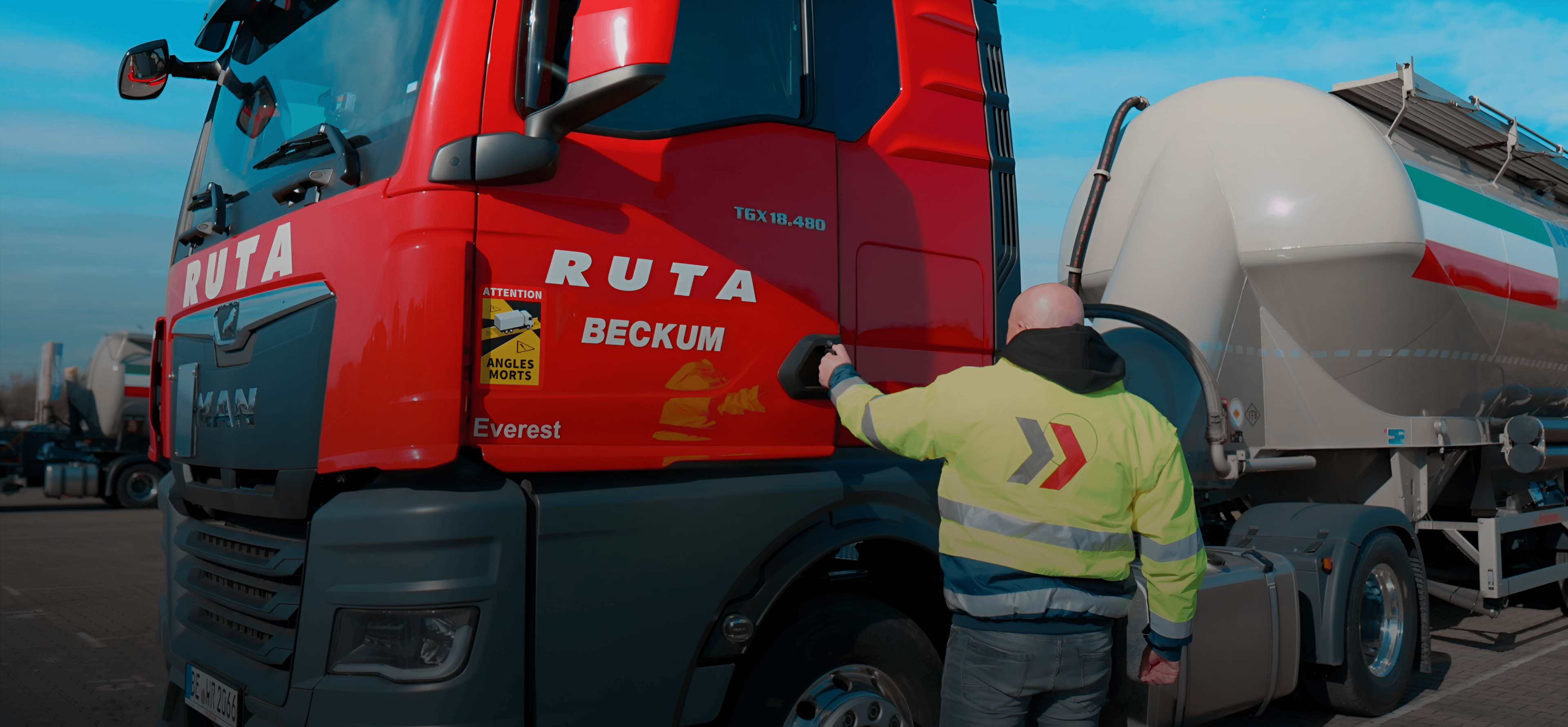 Kraftfahrer der Werner Ruploh Unternehmensgruppe steht neben einem roten RUTA-LKW und legt die Hand an die Fahrertür.