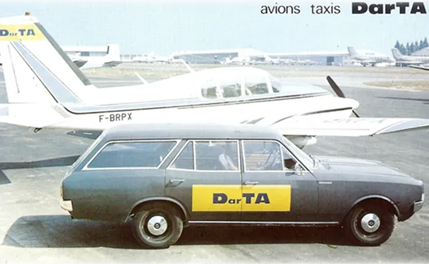Voiture noire avec une pancarte jaune DarTA garée sur un tarmac d'aéroport, devant un petit avion blanc immatriculé F-BRPX.