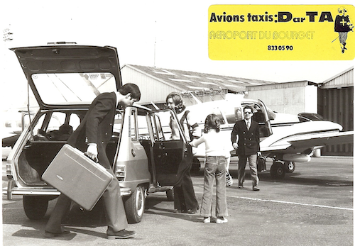 Un homme portant une valise ouvre le coffre d'une voiture, une femme tient la porte arrière ouverte pour une autre femme et un enfant devant un petit avion sur un tarmac.