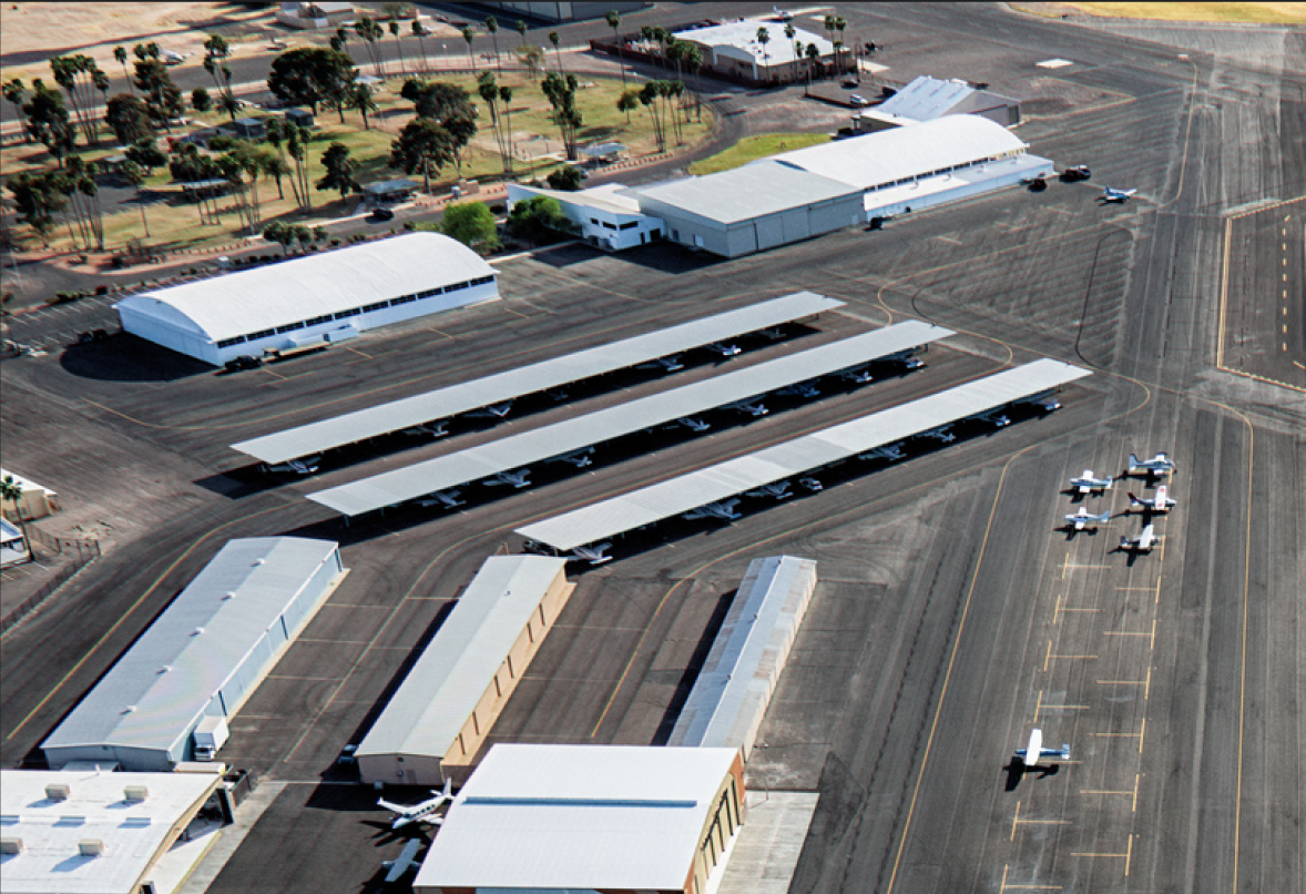 Vue aérienne d'un aéroport avec plusieurs hangars, de petits avions garés sous des abris et sur le tarmac.