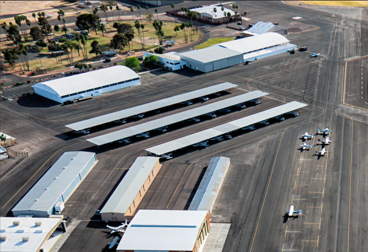 Vue aérienne d'un aéroport avec plusieurs hangars, de petits avions garés sous des abris et sur le tarmac.