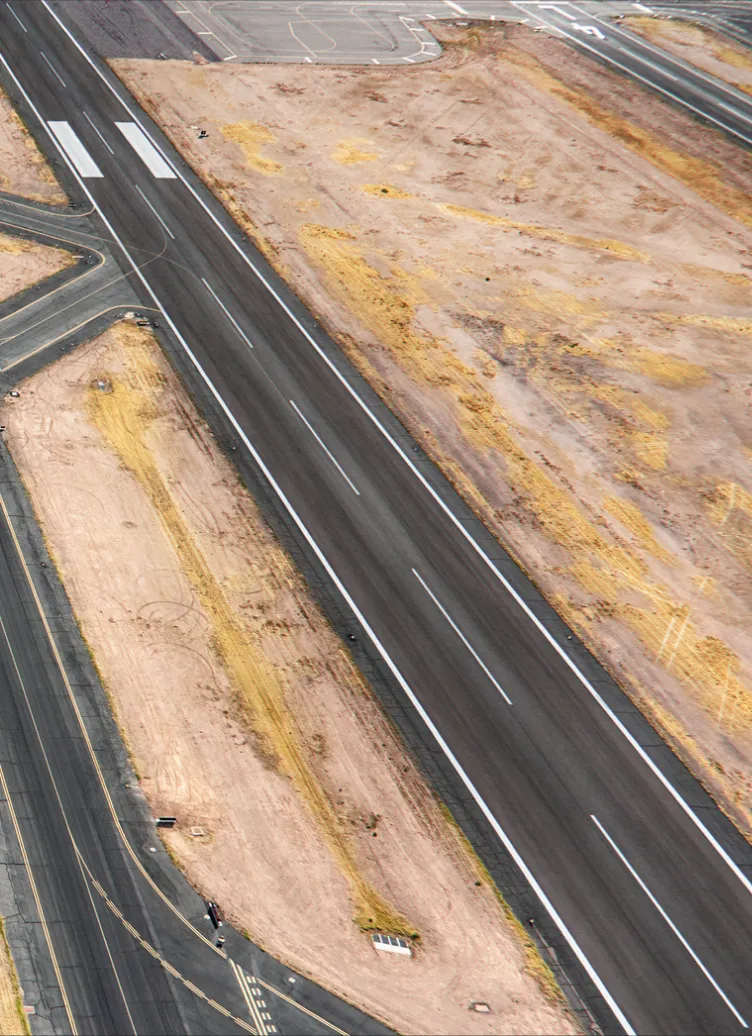 Vue aérienne d'une piste d'atterrissage d'aéroport entourée de zones de terre et voies de circulation.