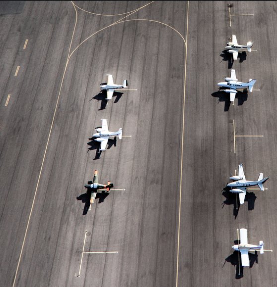 Vue aérienne de plusieurs petits avions stationnés en rangées sur une piste d'aéroport.