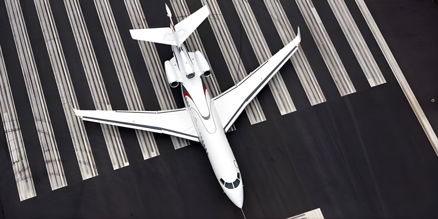 Vue aérienne d’un avion d'affaires privé blanc stationné sur une piste d’aéroport avec des marques de piste visibles.