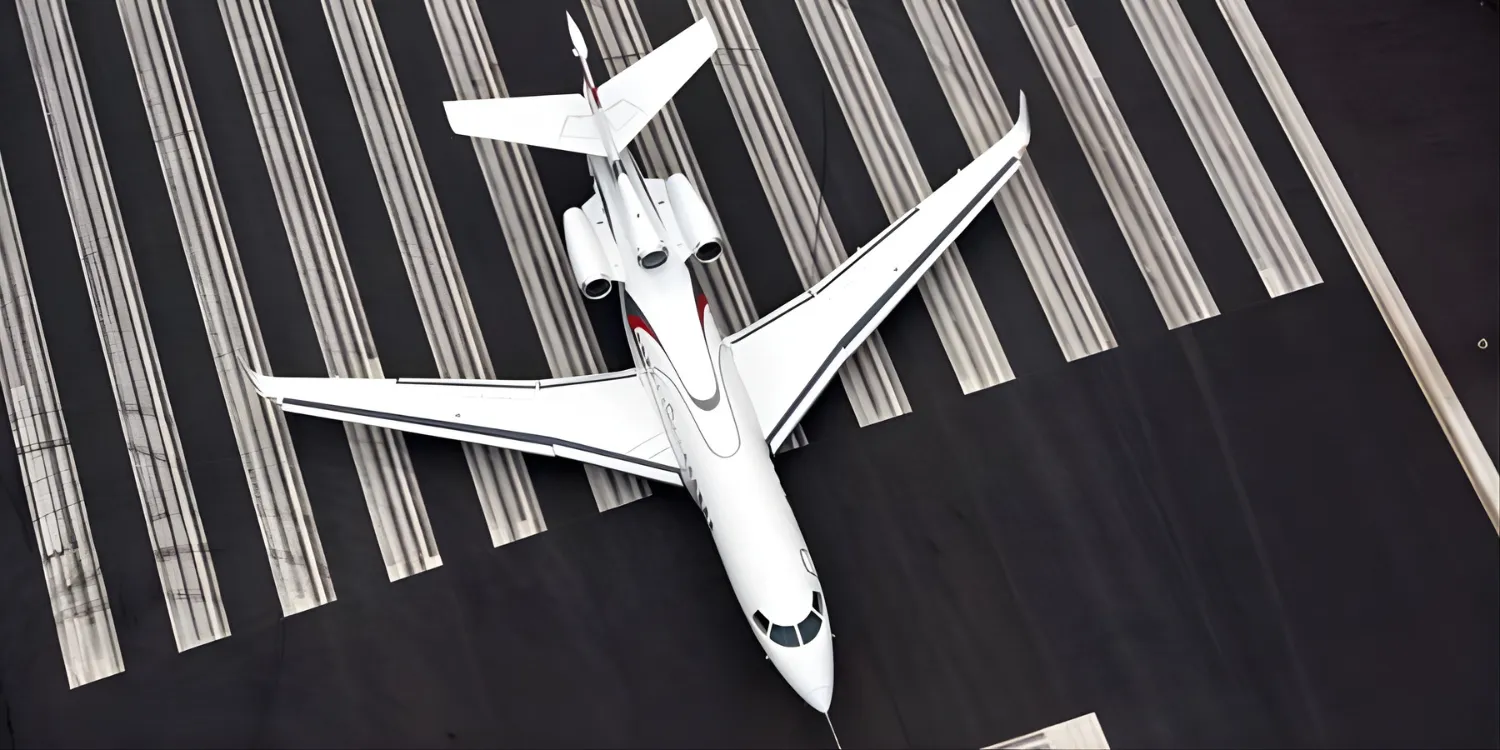 Vue aérienne d’un avion d'affaires privé blanc stationné sur une piste d’aéroport avec des marques de piste visibles.