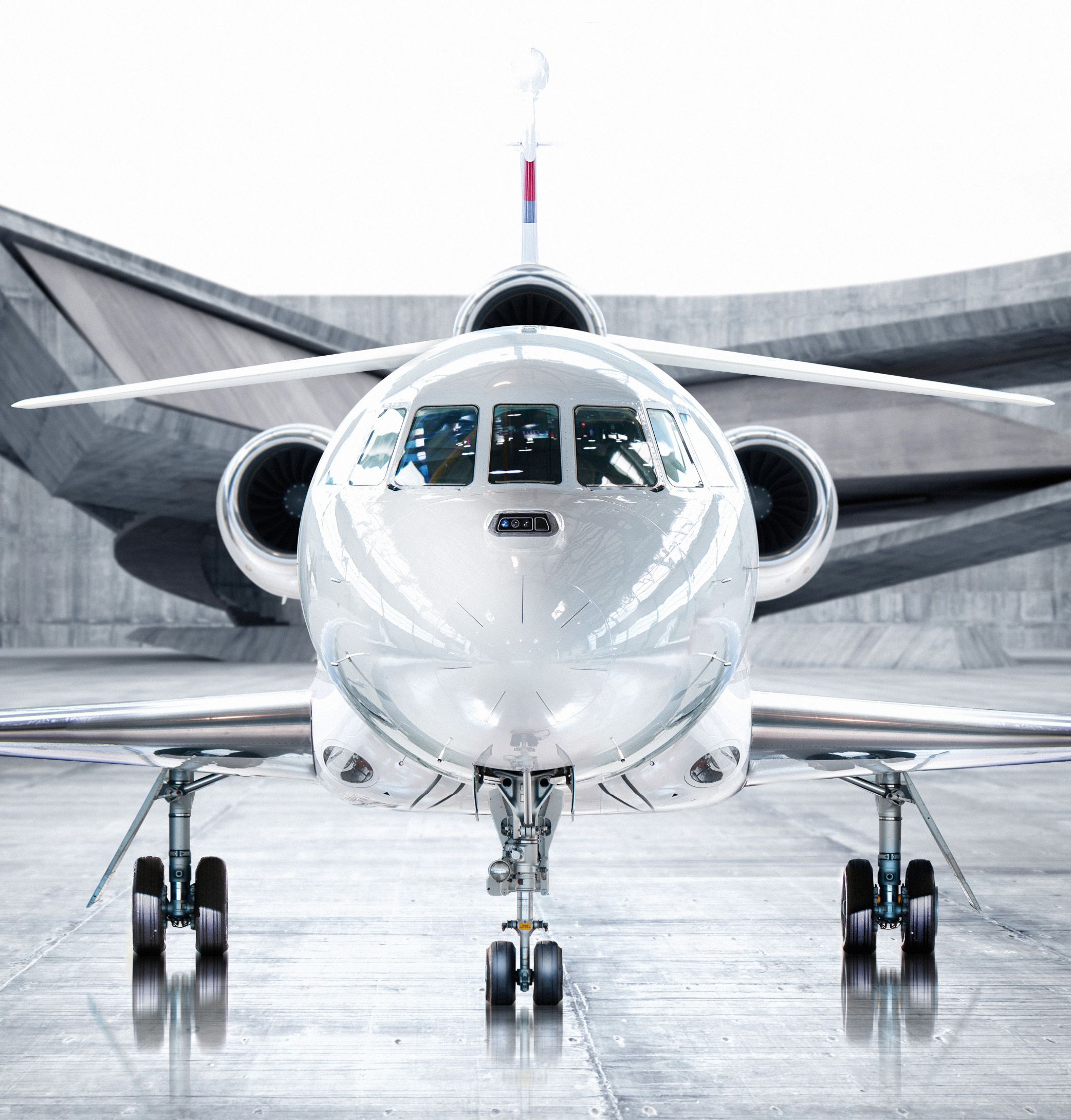 Vue frontale d’un avion d'affaires privé blanc dans un hangar moderne avec un fond en béton géométrique.
