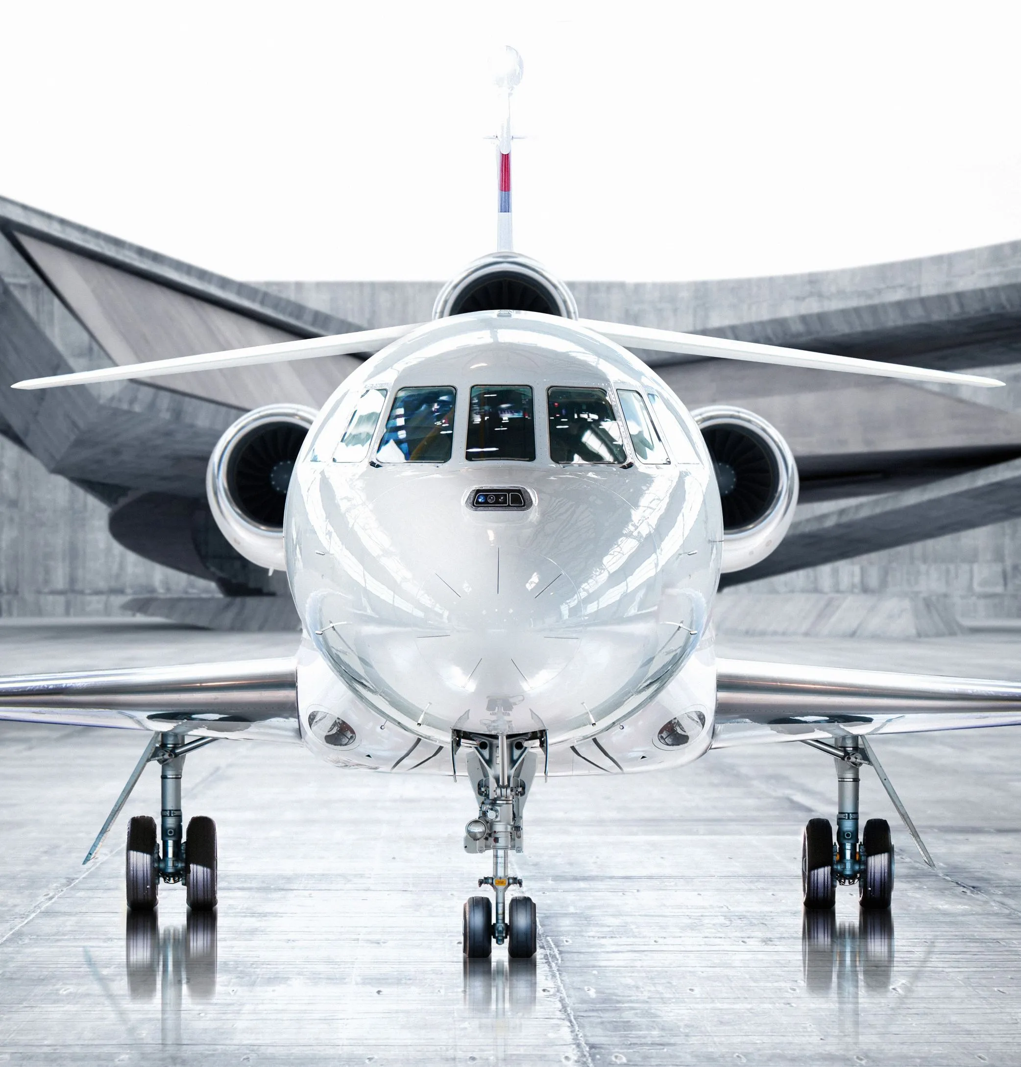 Vue frontale d’un avion d'affaires privé blanc dans un hangar moderne avec un fond en béton géométrique.
