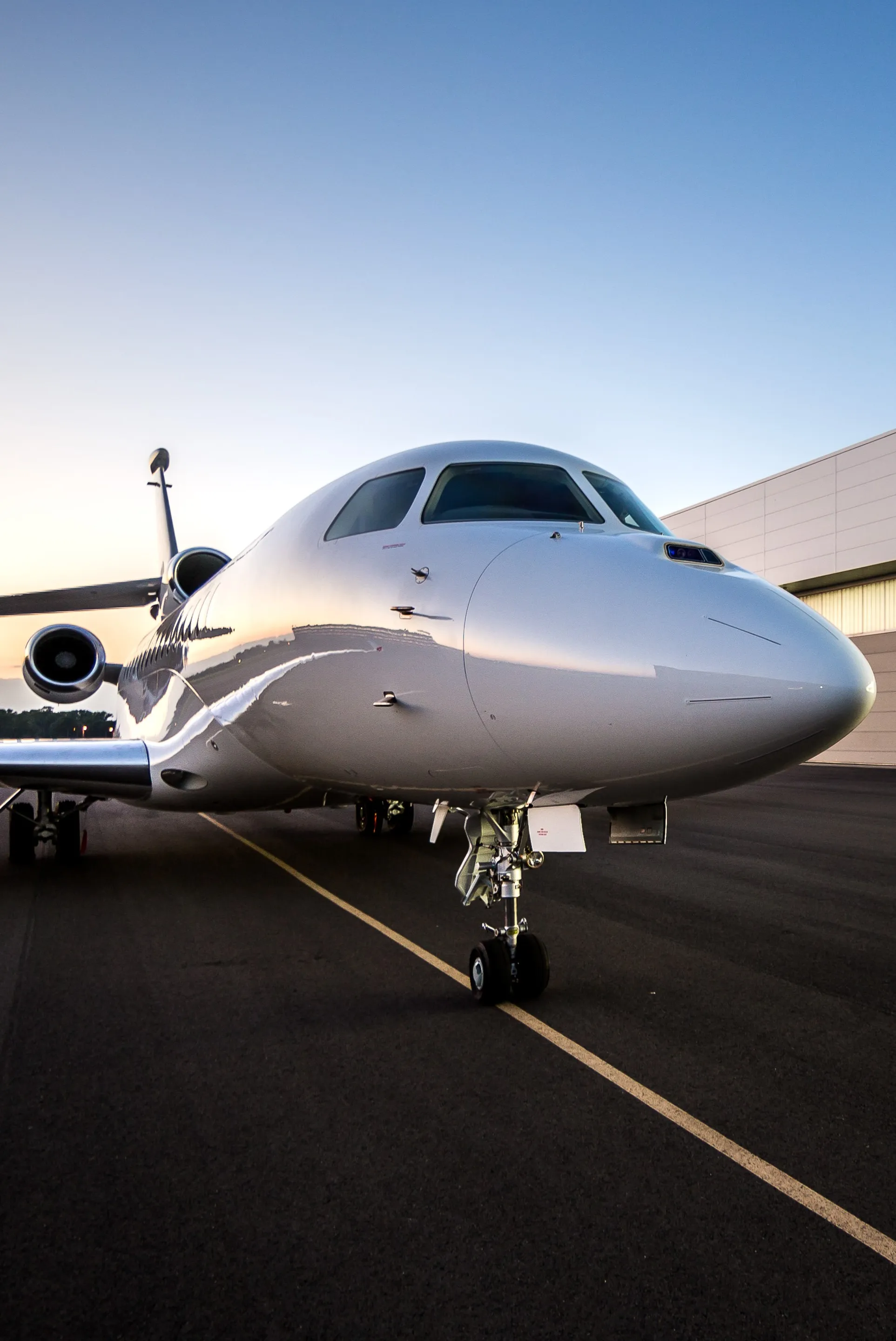 Avion d’affaires blanc stationné sur un tarmac au coucher du soleil.