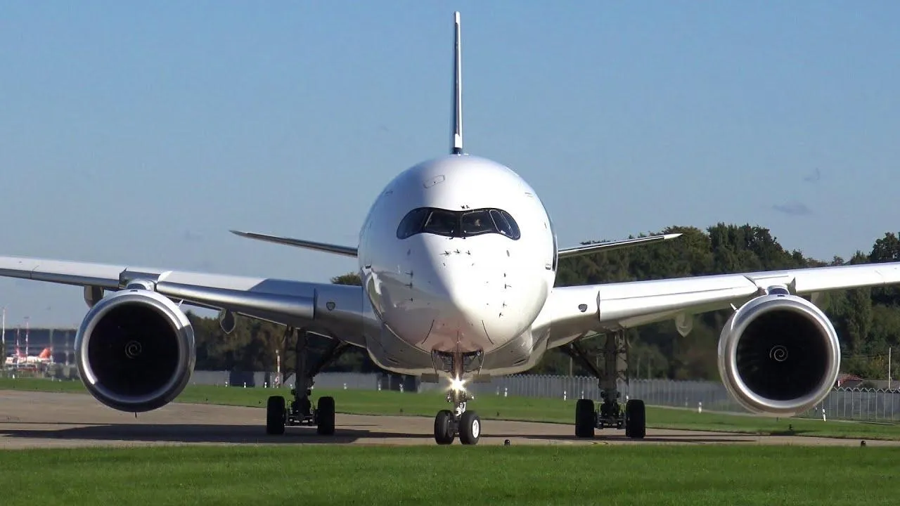 Vue frontale d'un avion commercial blanc sur une piste d'aéroport avec un ciel bleu clair.