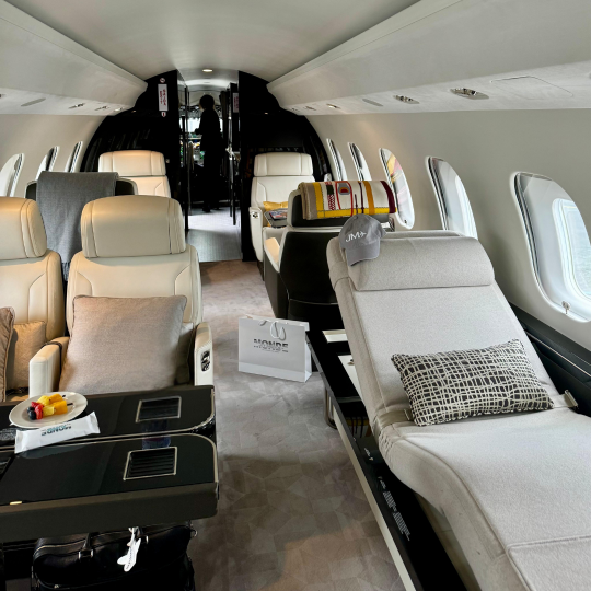 Intérieur spacieux et luxueux d'un jet privé avec sièges en cuir crème, une chaise longue, plusieurs fenêtres ovales et une table noire avec des encas.