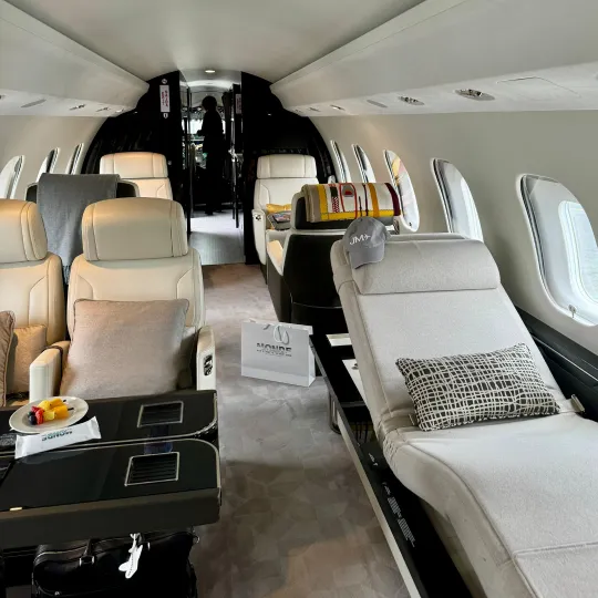 Intérieur spacieux et luxueux d'un jet privé avec sièges en cuir crème, une chaise longue, plusieurs fenêtres ovales et une table noire avec des encas.