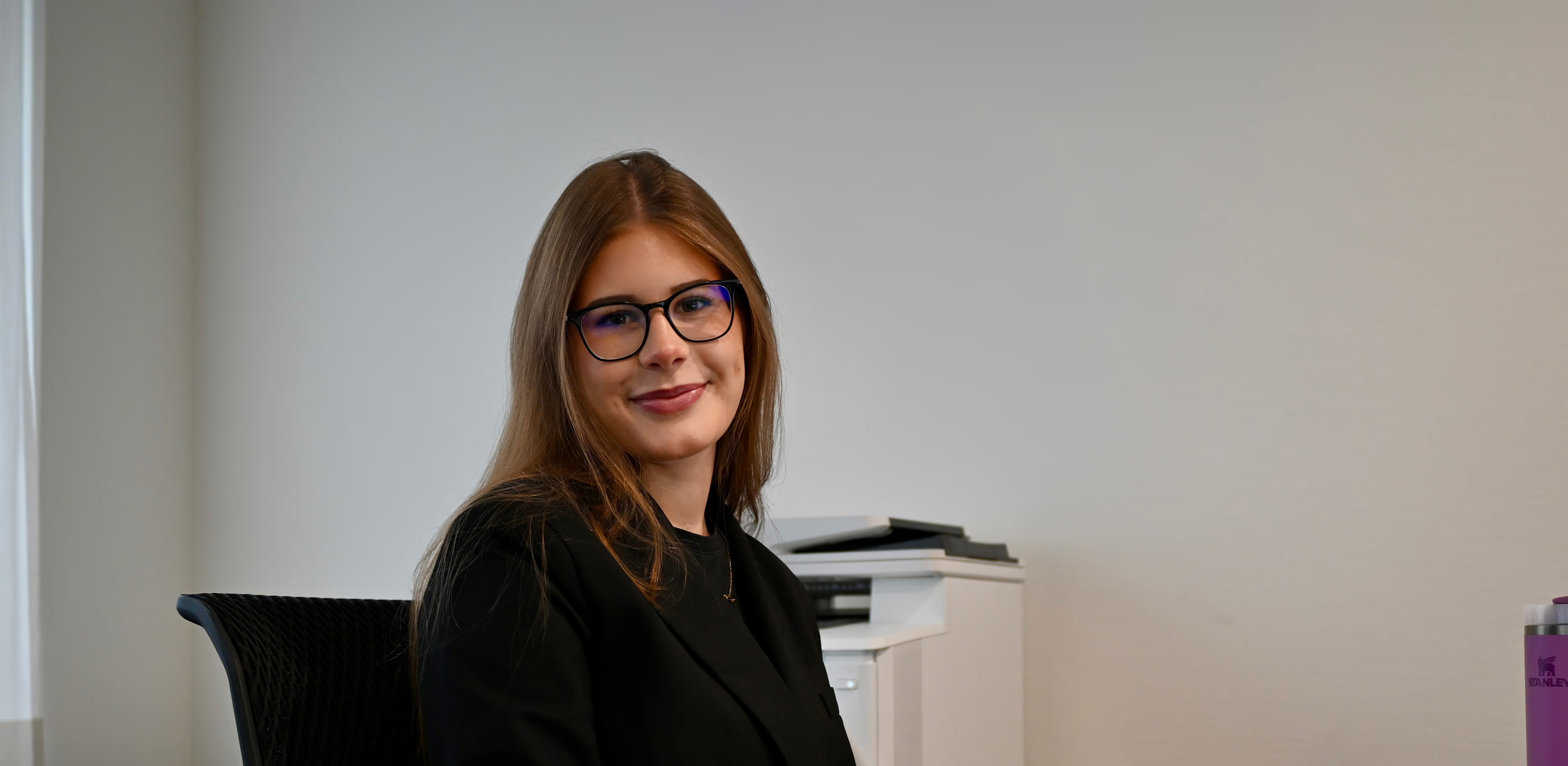 Eine Dame sitzt am Arbeitsplatz und lächelt in die Kamera.