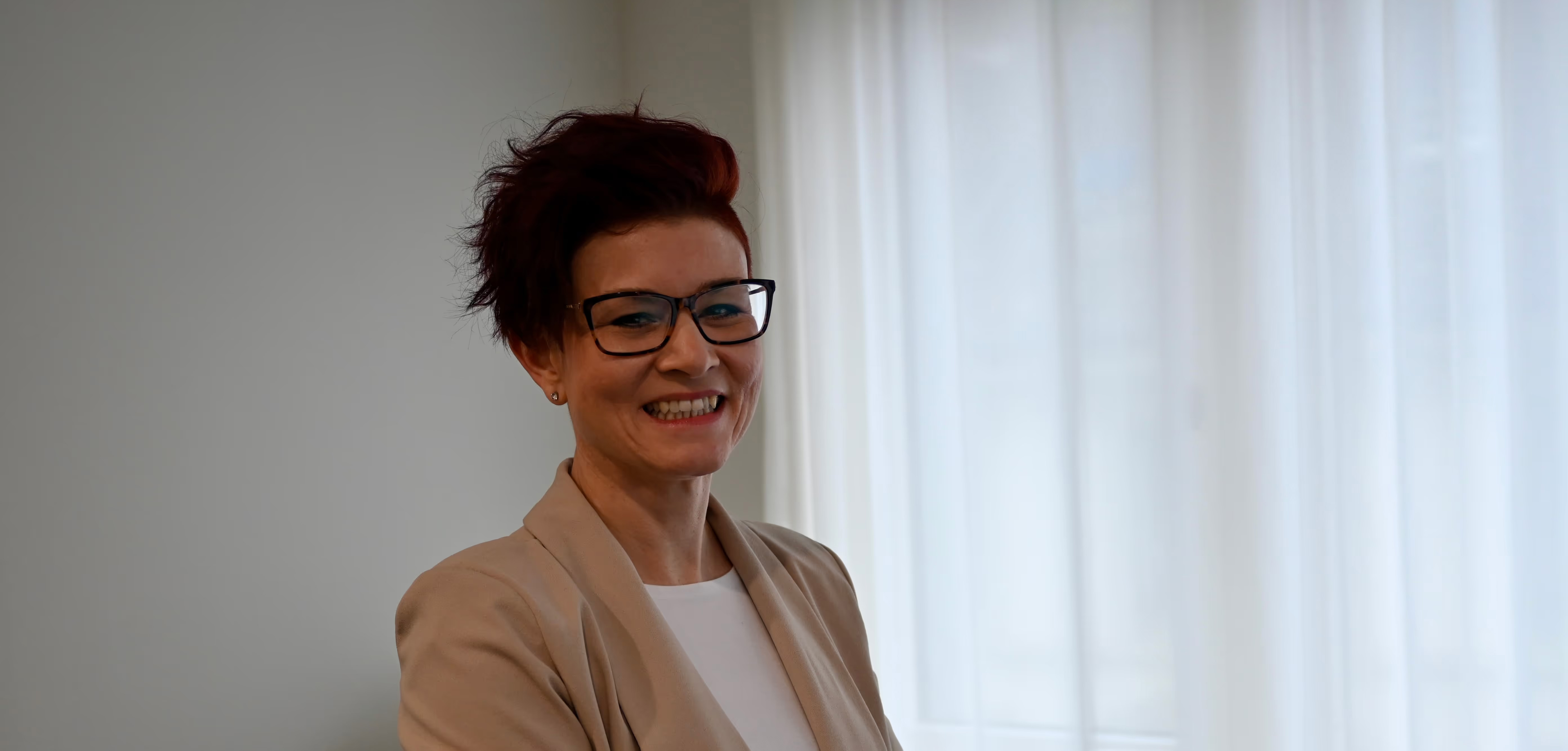 Eine Dame sitzt am Arbeitsplatz und lächelt in die Kamera.