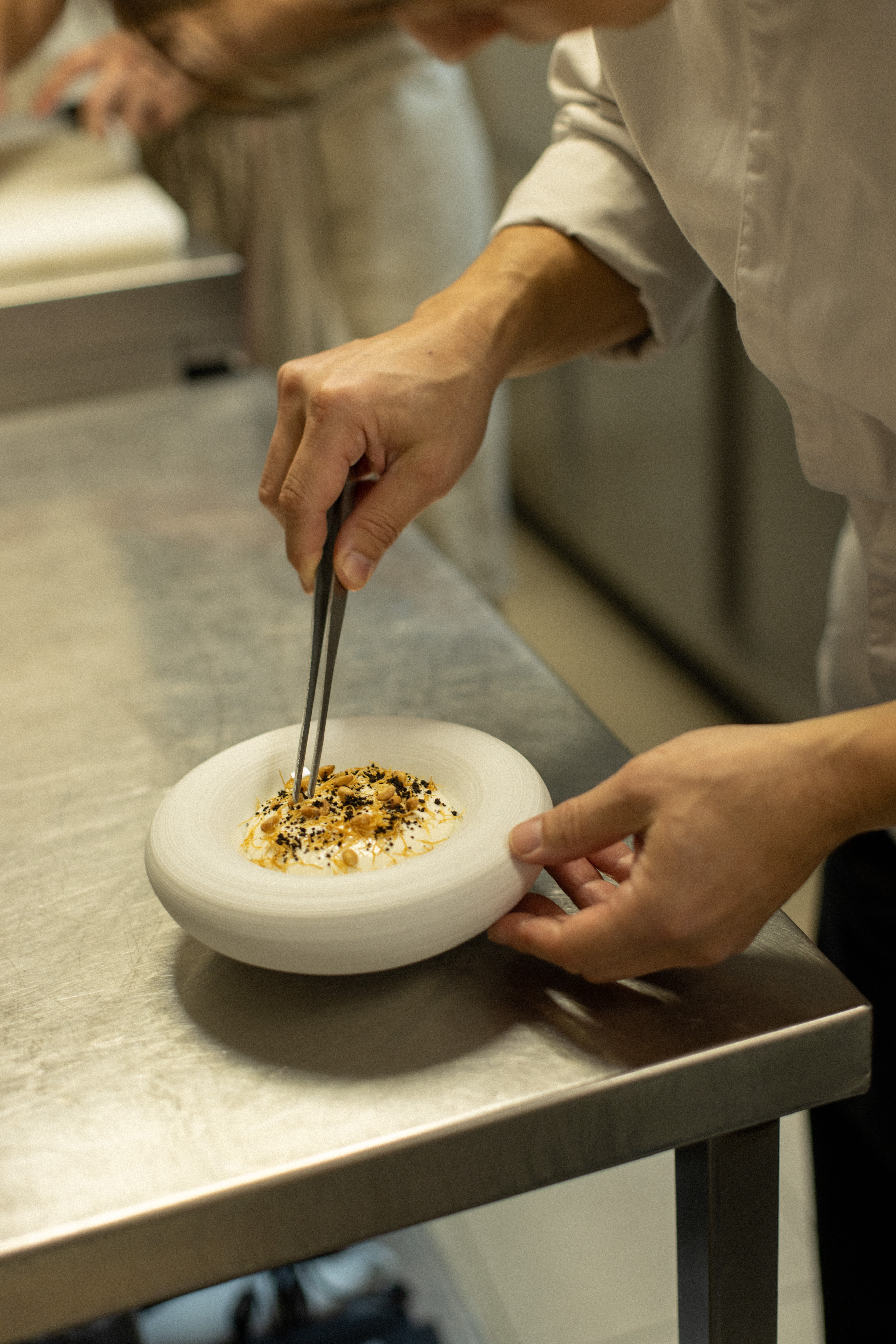 Chef Kunihisa Goto dressant une assiette gastronomique dans la cuisine de L’Axel Restaurant, restaurant étoilé reconnu pour son attention aux détails et à l’expérience client.