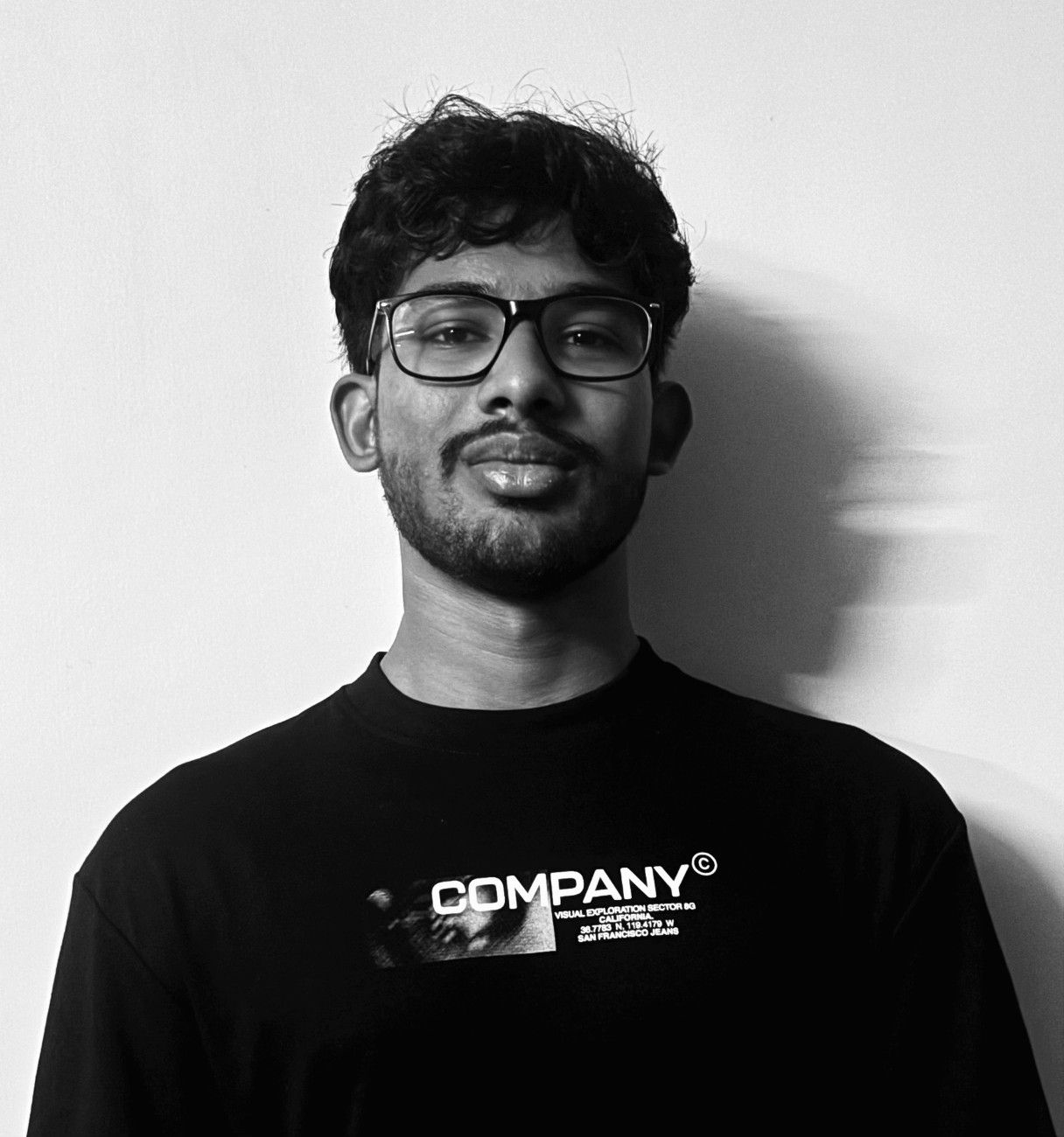 Portrait of a man with glasses and curly hair wearing a black T-shirt with white text reading COMPANY.