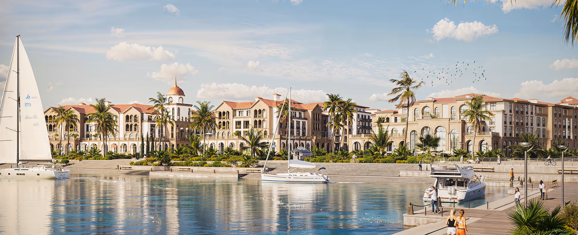 A sailboat in the water next to a large building - marina village