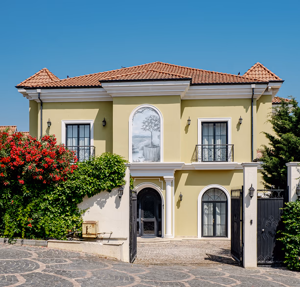 A yellow house with a red flowered bush in front of it - villa siena