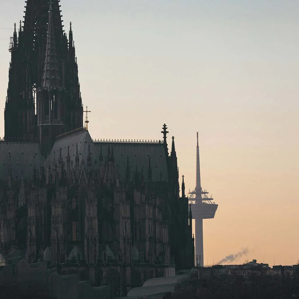 Silhouette des Kölner Doms mit dem Rheinturm im Hintergrund bei Sonnenuntergang.