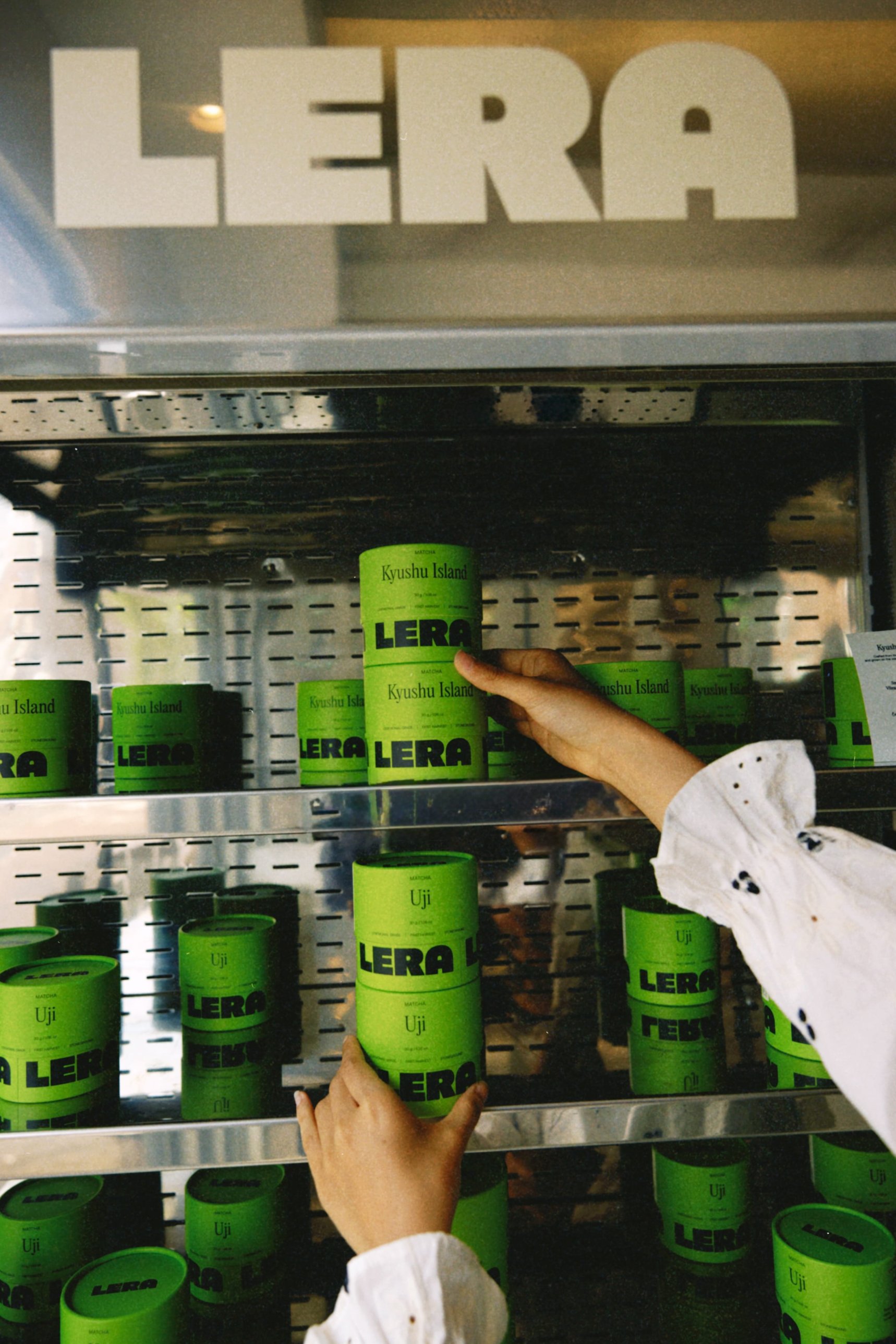 Hands placing LERA Kyushu Island and Uji matcha tins on a shelf